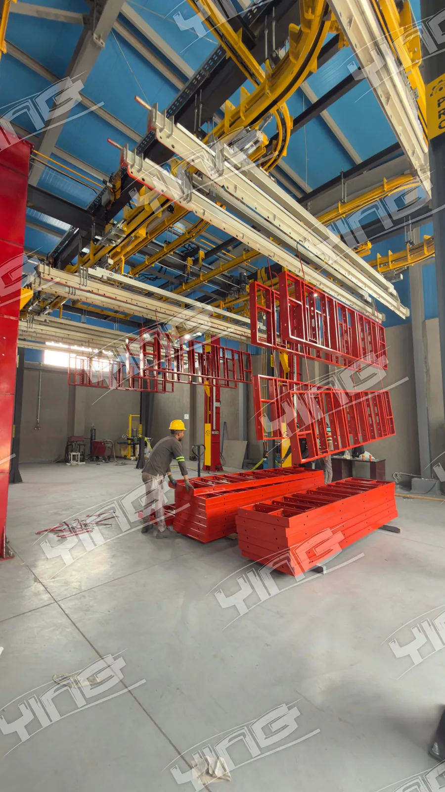 Coated red scaffolding frames at the loading area beneath the overhead power and free conveyor