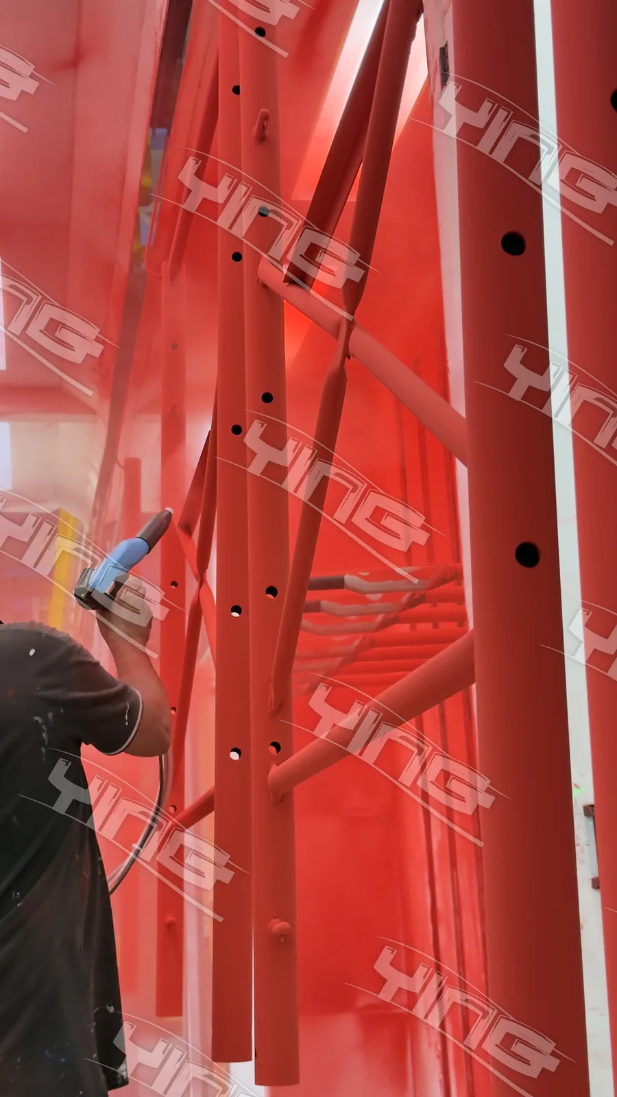 Operator spraying red powder onto scaffolding frames in the powder booth